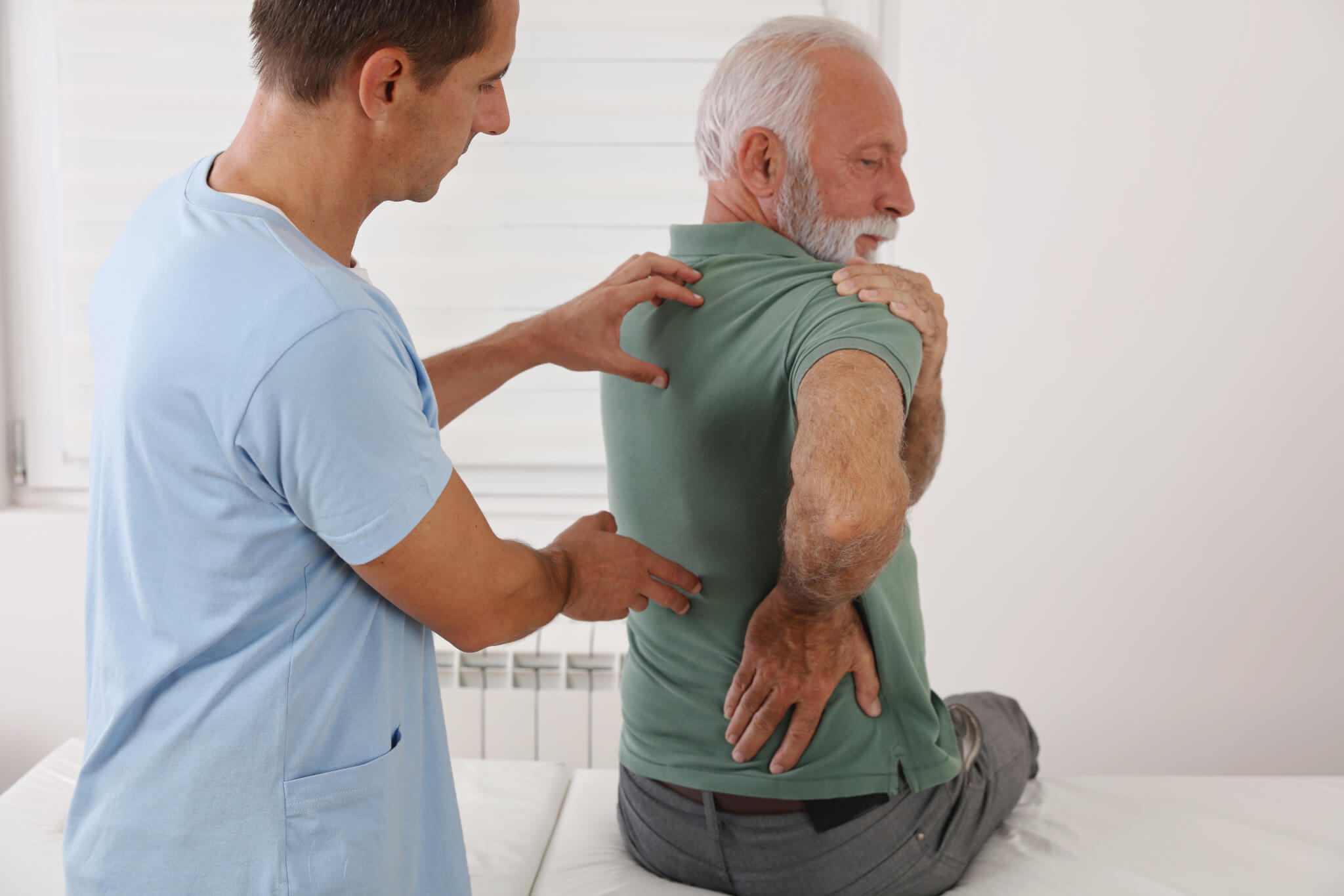 A healthcare provider examines an elderly man with chronic back pain